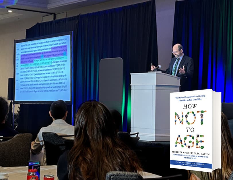 Dr. Greger at a white podium next to his presentation slides on a screen