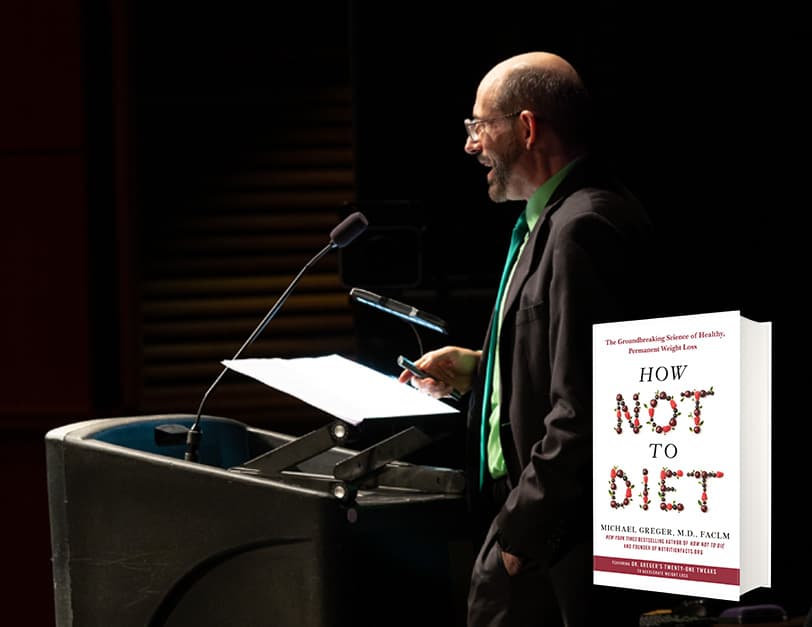 Dr. Greger speaking at a podium under a spotlight