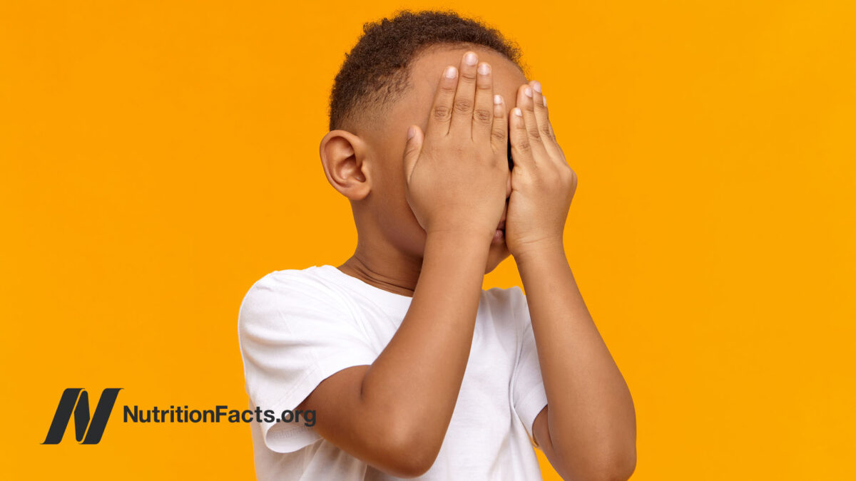 young boy covering his face against orange background