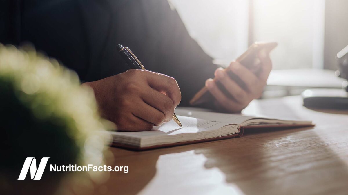 Image of man writing notes in a journal while referencing his phone screen