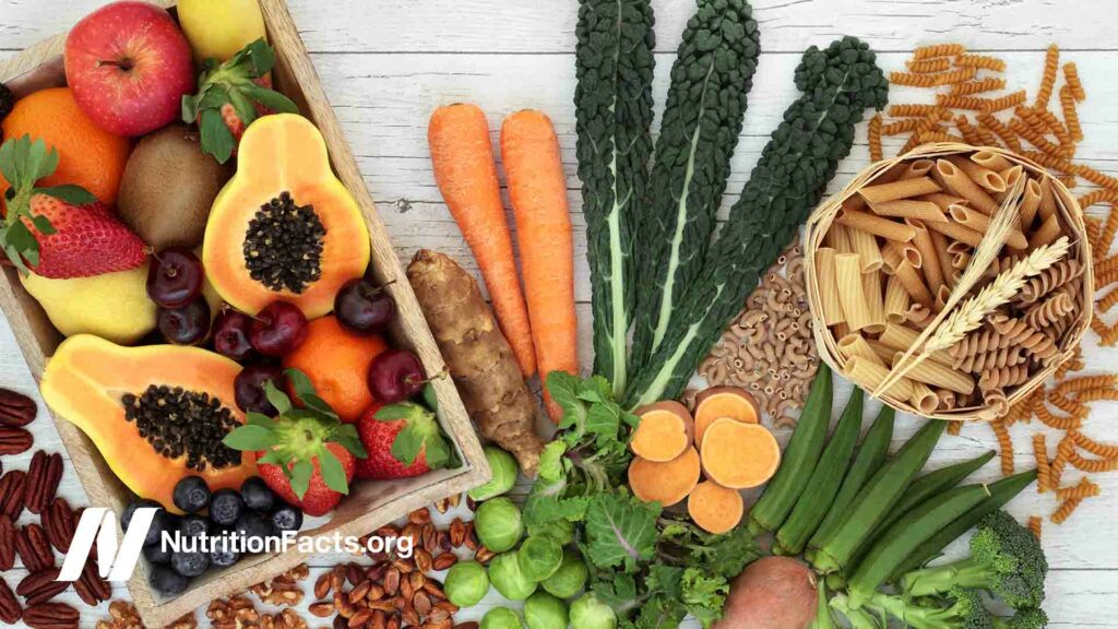 Alimentos de origen vegetal ricos en fibra con pasta integral, frutos secos, frutas y verduras sobre un fondo rústico