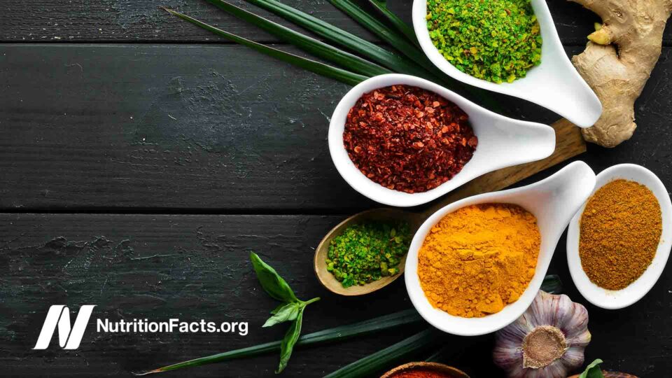 Collection of spices and herbs in bowls and spoons on a black wooden background