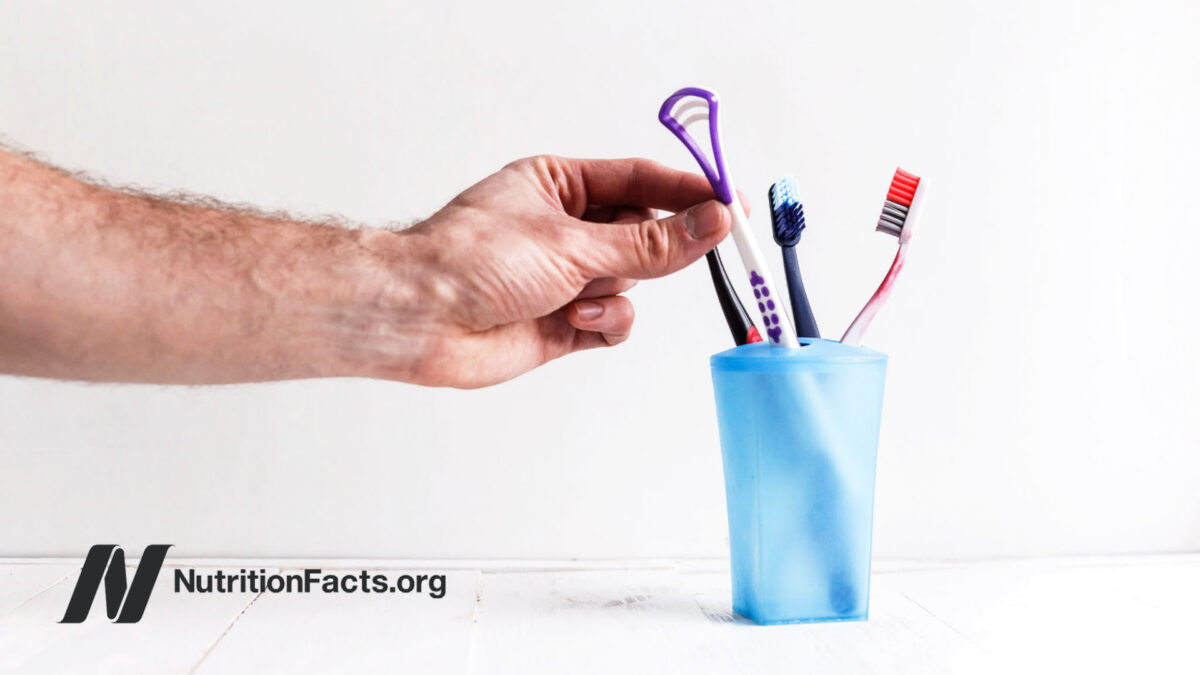 Hand reaching for a tongue scraper out of a cup of assorted dental tools