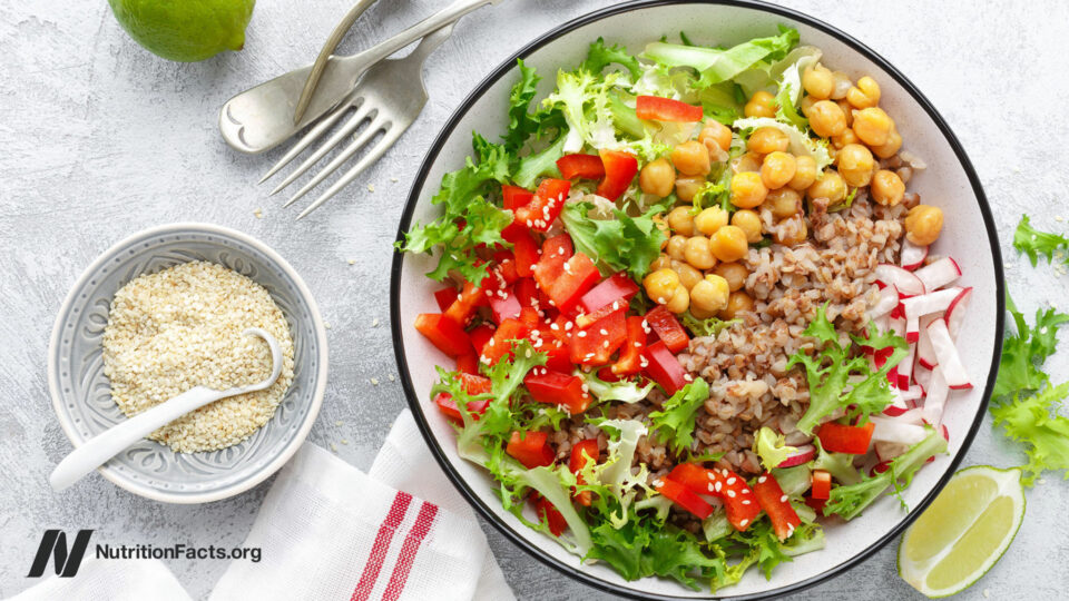 Round bowl of beans, greens, and other whole foods on a white surface