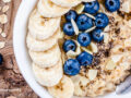 Oatmeal in a bowl on a wood surface with banana and blueberries