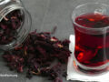 Glass of steeping hibiscus tea and loose leaf laying around