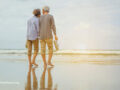Senior couple walking on the beach holding hands and barefoot at sunrise