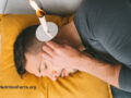 Person lying on their side with a candle over their ear