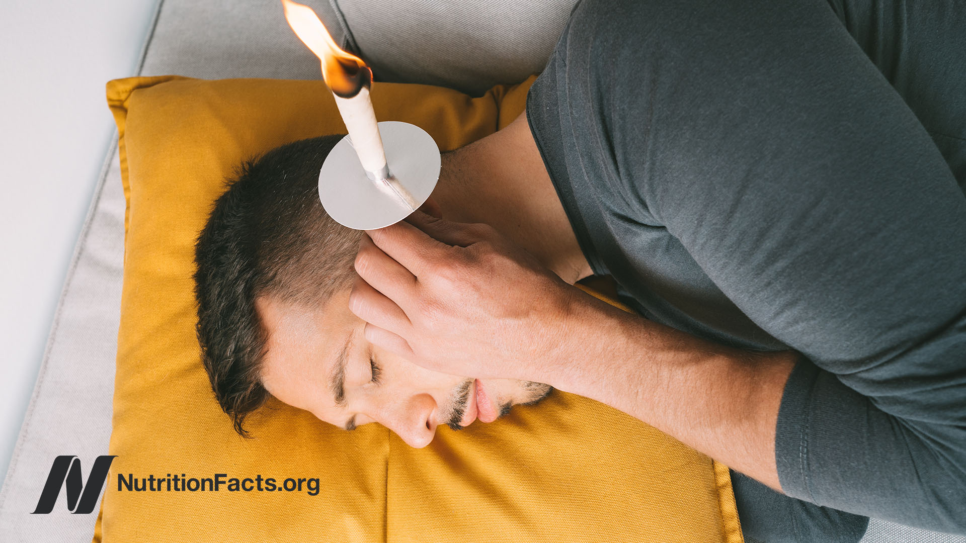 Person lying on their side with a candle over their ear