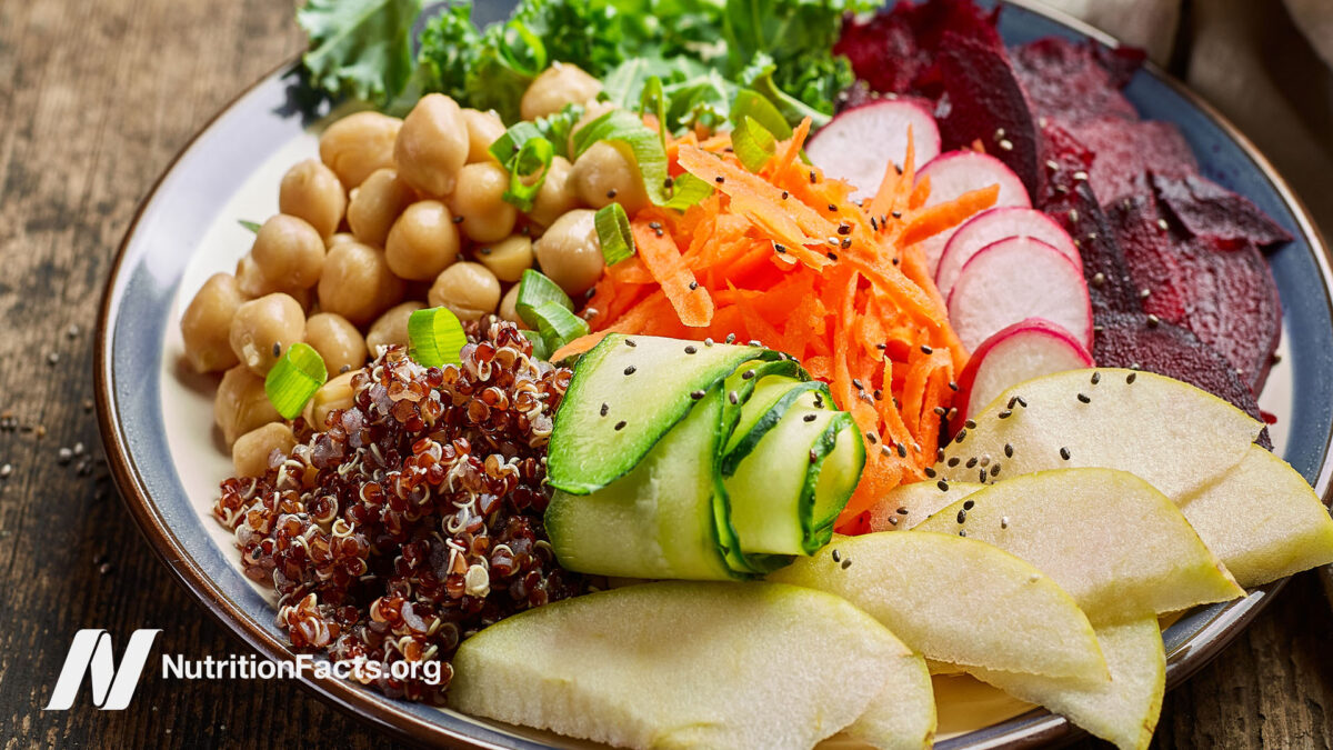 ​​Plant based dish in a bowl, containing shredded carrots, cucumber, turnips, beets, kale, apple slices, and cooked quinoa