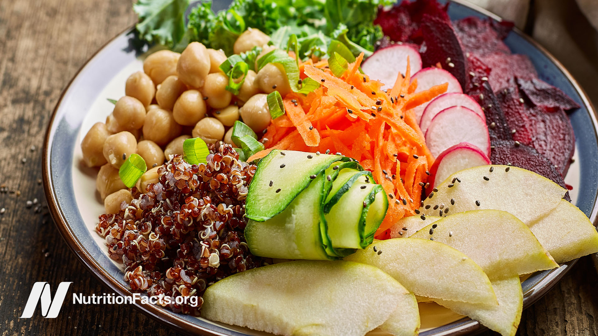 ​​Plant based dish in a bowl, containing shredded carrots, cucumber, turnips, beets, kale, apple slices, and cooked quinoa