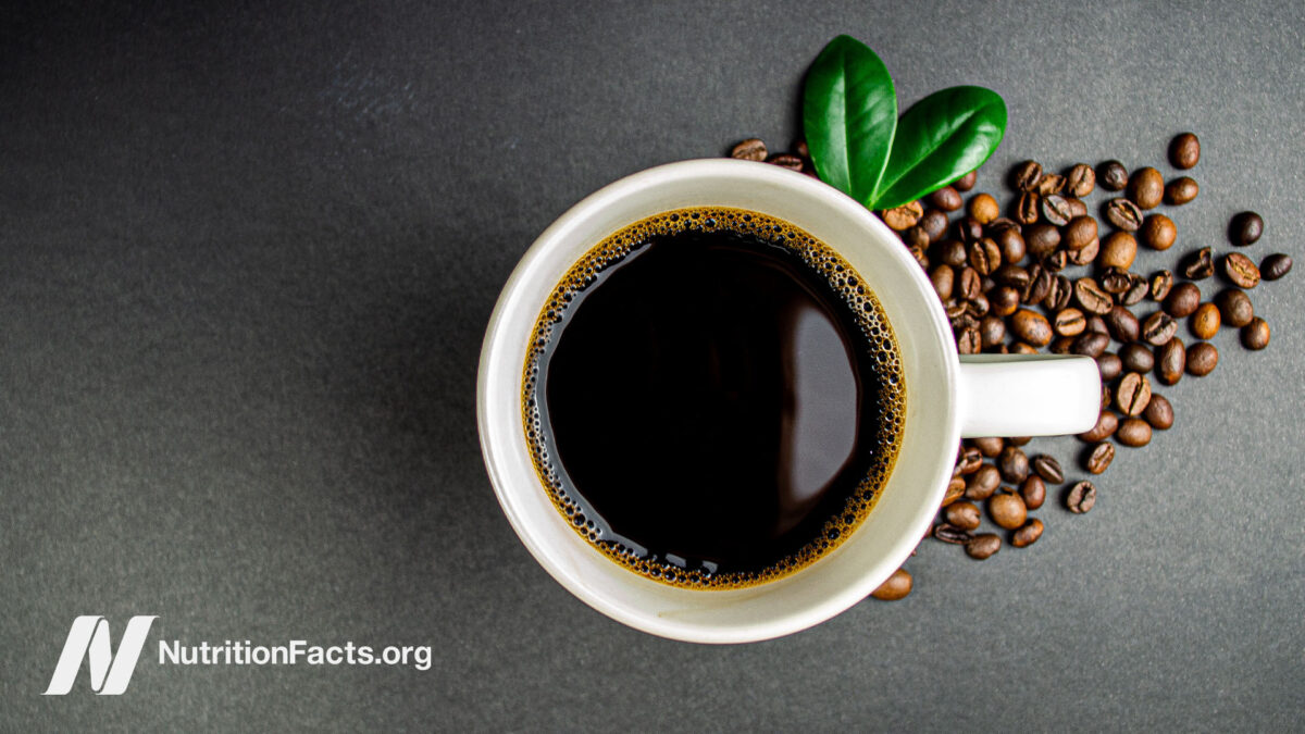 Close birds-eye view of a ceramic cup of coffee with coffee beans scattered beside the cup