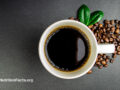 Close birds-eye view of a ceramic cup of coffee with coffee beans scattered beside the cup