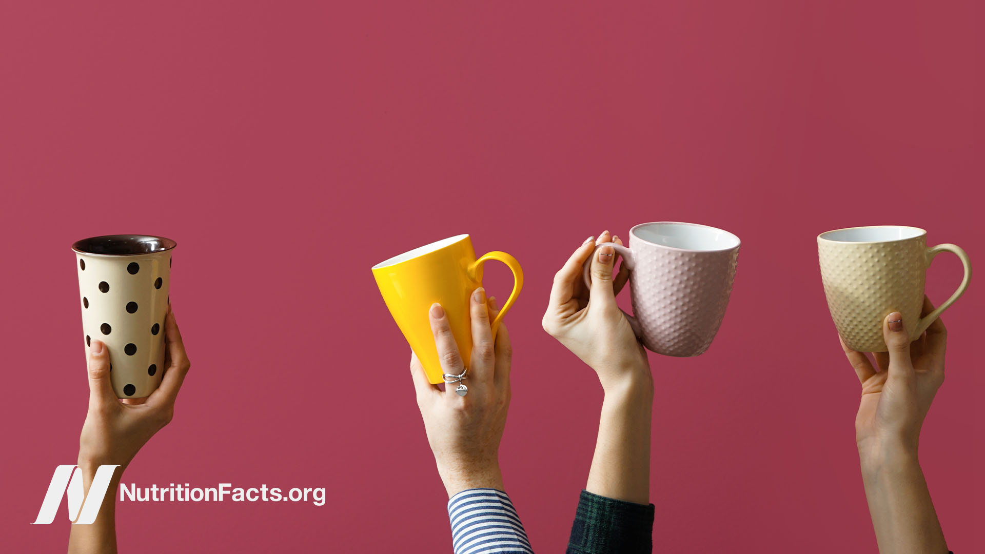 Four hands holding up different style mugs of coffee in front of a deep red berry background