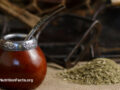 Close up view of a yerba mate gourd, also known as a bombilla, used to drink loose leaf yerba mate with a metal straw next to a small pile of yerba mate
