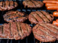 Close up view of hamburgers and hotdogs cooking on the grill.
