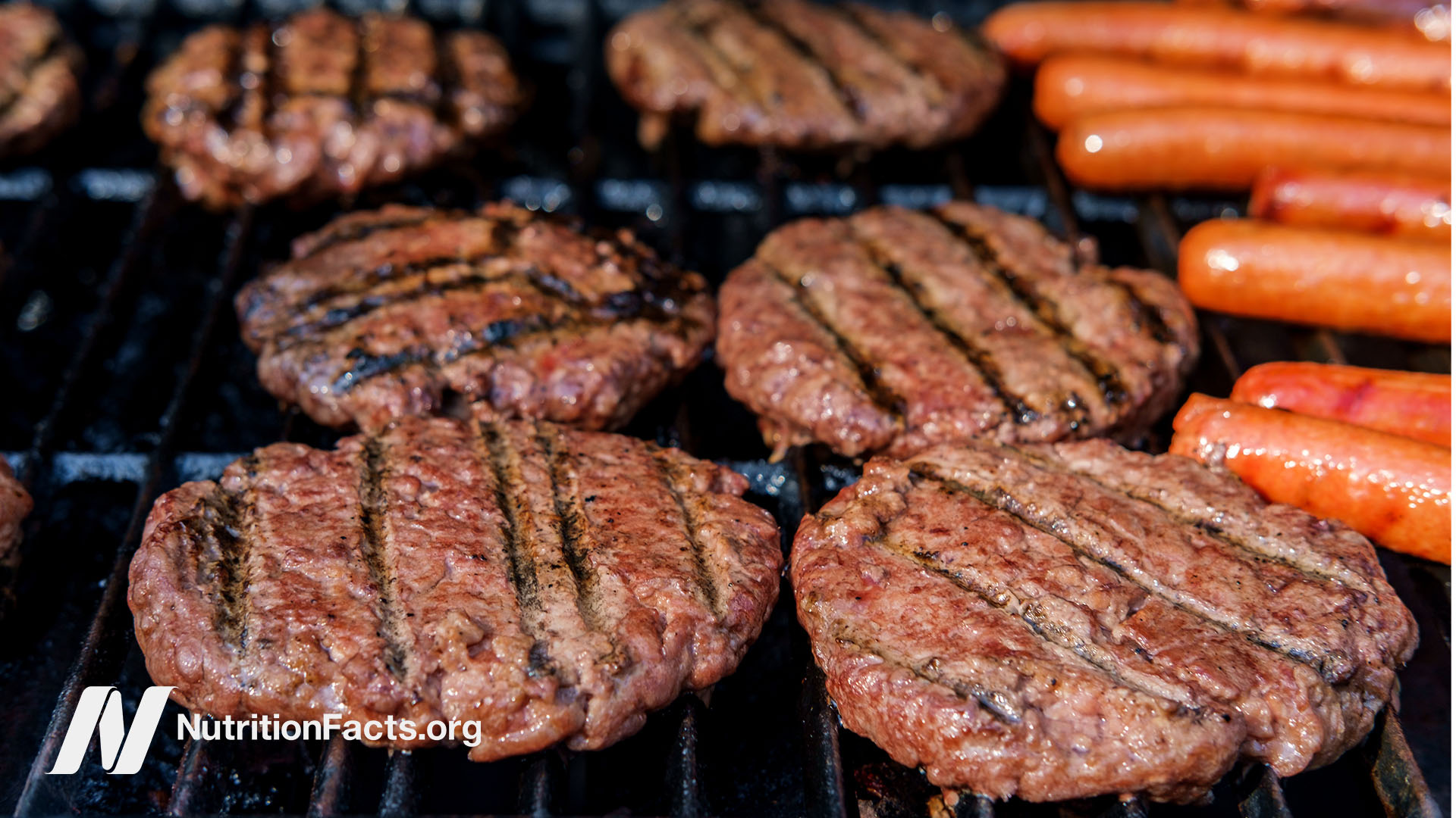 Close up view of hamburgers and hotdogs cooking on the grill.