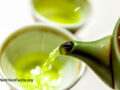 Close up view of a deep green tea pot pouring hot green tea into a mug