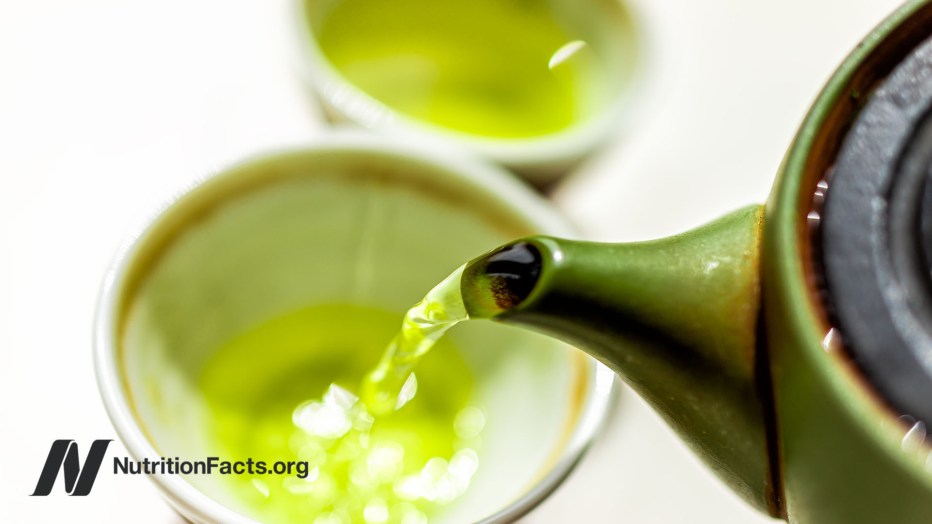 Close up view of a deep green tea pot pouring hot green tea into a mug
