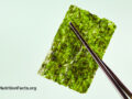 Dark wooden chopsticks holding up a dried seaweed nori sheet in front of a light