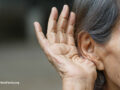 Elderly person holding their hand up to their ear