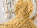 Large glass jar pouring out a pile of nutritional yeast