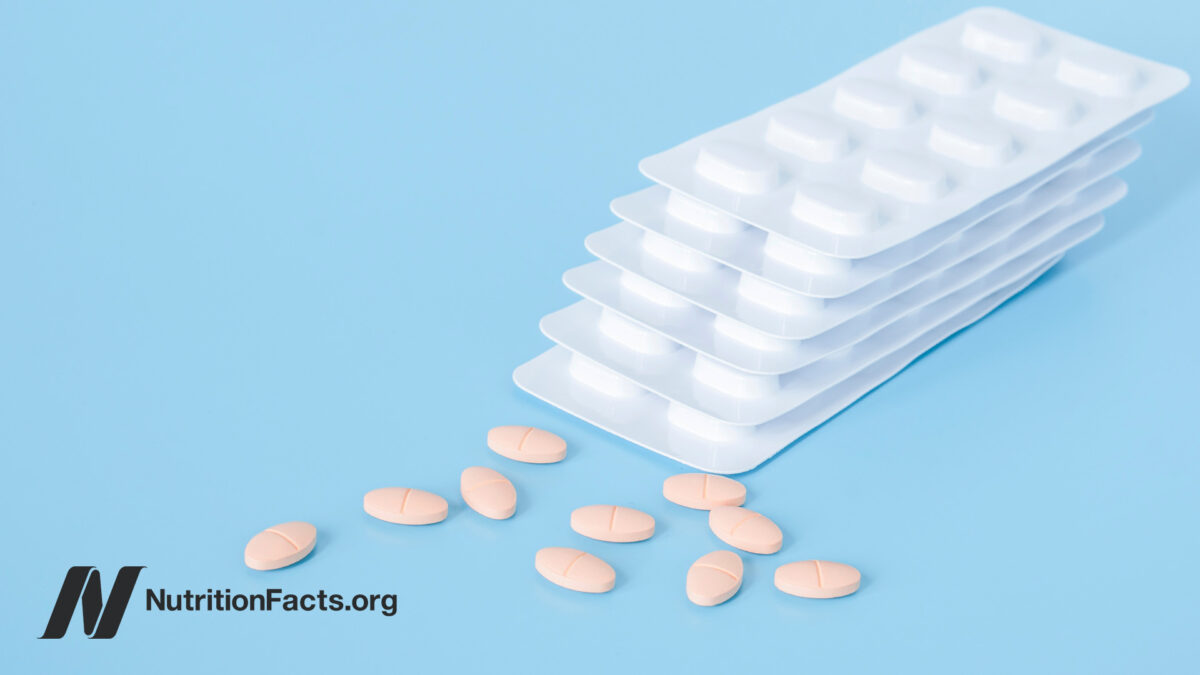 Pink tablets of statins next to a small pile of tablet sheets in front of a blue background