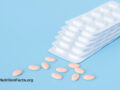 Pink tablets of statins next to a small pile of tablet sheets in front of a blue background