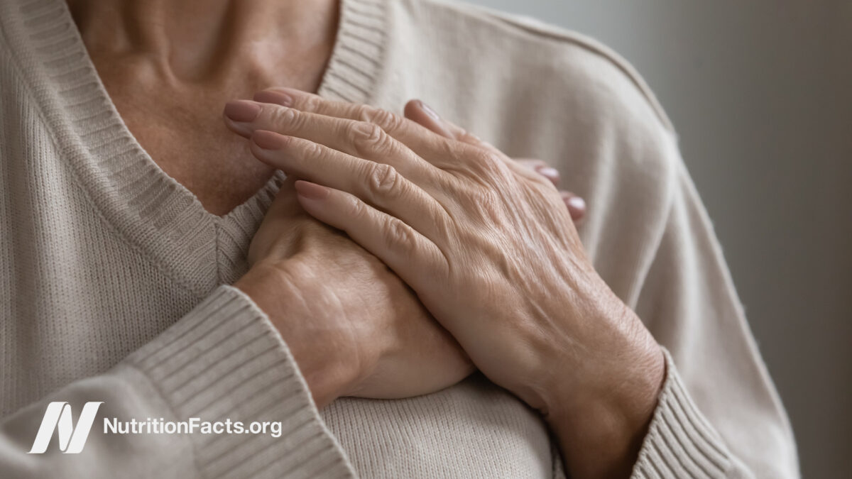 Elderly person wearing a sweater holding both hands to their chest