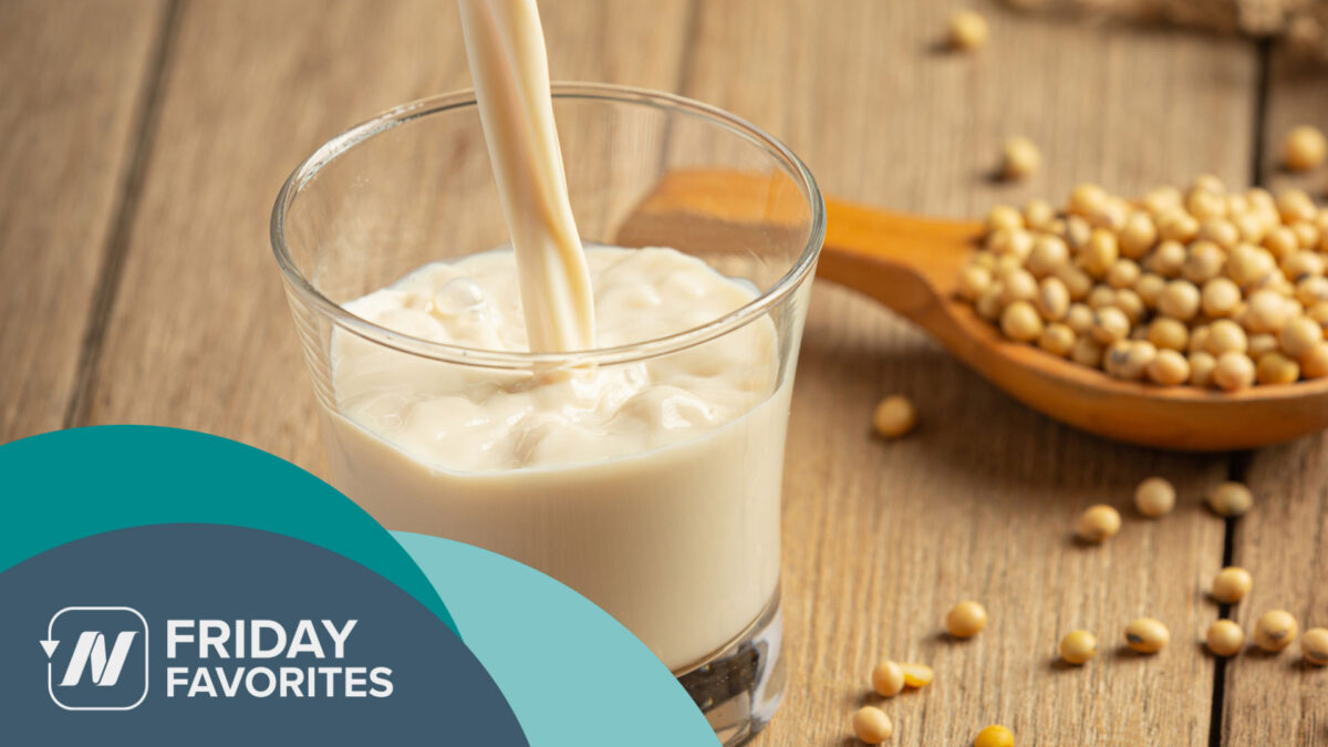 a glass being filled with soy milk and a wooden spoon filled with dry soy beans beside