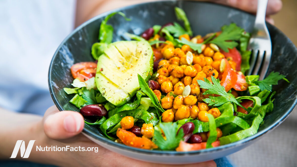 Person holding a salad bowl filled with greens, chickpeas, tomatoes, and avocado