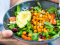 Person holding a salad bowl filled with greens, chickpeas, tomatoes, and avocado