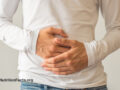 Person with a long sleeved white shirt and jeans holding their hands over their stomach