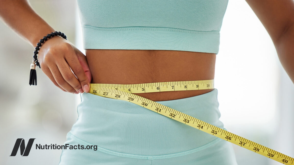 Person wearing teal workout gear measuring their waist with a yellow measuring tape