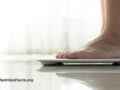Feet placed on a weight scale from the side in front of a light background