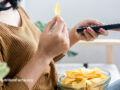Side view of a person sitting on a couch with a bowl of potato chips on their lap