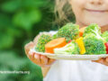 Child holding out a plate of fresh vegetables